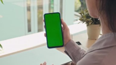 Akıllı telefonun önünde, ev ofisinin arka planında yeşil renkli ekranlı, yavaş çekimde konuşan kadının yakın plan görüntüsü.