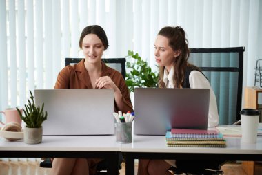 Dizüstü bilgisayarda çalışan ve masada otururken online projeyi tartışan genç meslektaşlar