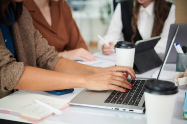 Ofiste iş arkadaşlarıyla masada otururken bilgisayarında daktilo yazan iş kadınının yakın çekimi.