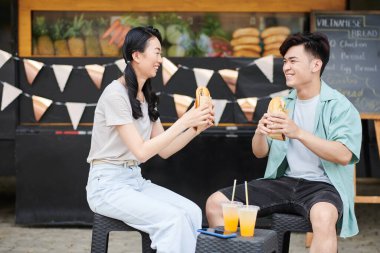 Genç, neşeli Asyalı randevular günlük kıyafetlerle dışarıda lezzetli sosisliler yerken mola yerinde fast food kamyonunun karşısında oturup sohbet ediyorlar.