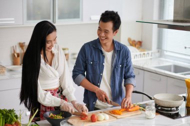 Mutlu genç Asyalı çift sohbet ederken mutfak masasında durup kahvaltıda sebze salatası pişirirken ya da arkadaşlarıyla akşam yemeği yerken.