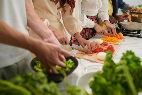 一排年轻的跨文化朋友站在桌旁做饭时 拿着锋利的小刀切碎新鲜蔬菜做沙拉 — 图库照片