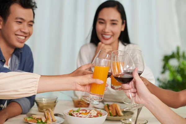 不同文化间的年轻朋友们的手与酒杯 红酒和橙汁杯在餐桌上互相碰碰 以对抗这对快乐的夫妇 — 图库照片