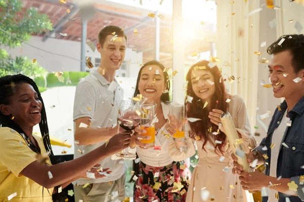 一群年轻而兴奋的不同文化间朋友一边喝着红酒 一边喝着葡萄酒和橙汁 一边享受着与五彩纸屑的家庭派对 — 图库照片