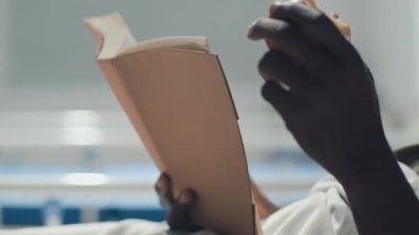Kafası kanayan Afrikalı Amerikalı asker kitap okuyor ve askeri hastanelerin koğuşunda yatağında meyve yiyor.