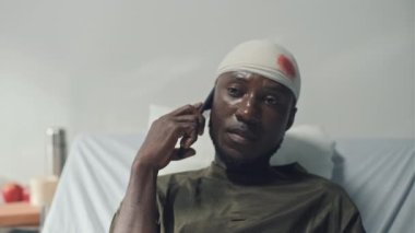 Askeri hastaneler koğuşunda yatakta yatarken kafasında yaralı bir şekilde telefonla konuşan Afrikalı Amerikan askerinin orta boy fotoğrafı.