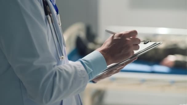 病院で頭部を出血させアフリカ系アメリカ人の軍人に署名するための文書を与える医師の中のショット — ストック動画