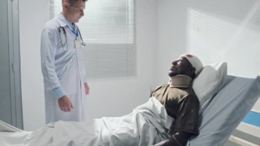 Beyaz üniformalı doktor elini sıkıyor ve askeri hastanenin koğuşunda yatarken kanaması olan asker destekliyor.