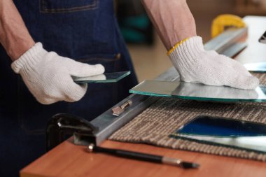 Eldiven giymiş, masa başında özel çalışma aleti olan cam parçalarından şekiller yapan işçilere yakın plan.