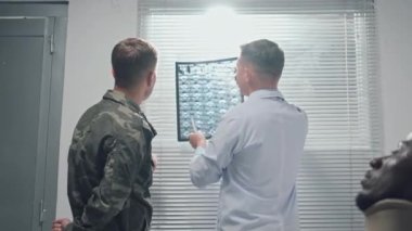 Beyaz önlüklü doktor ve asker askeri hastanenin koğuşunda yaralı bir hastanın röntgenini tartışıyor.