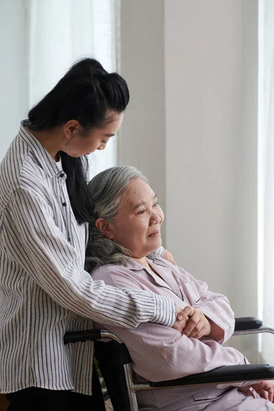 Vrouw Knuffelen Haar Senior Moeder Zitten Rolstoel Kijken Buiten — Stockfoto