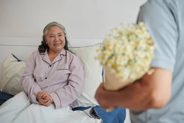 病院病棟で花と彼女の夫を見て幸せ病人シニア女性 — ストック写真