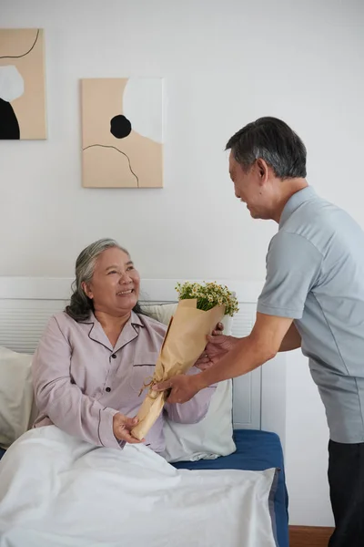 Fröhliche Kranke Seniorin Nimmt Blumen Von Ihrem Mann Entgegen — Stockfoto