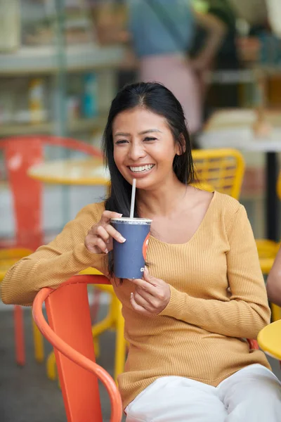 Śmiejąca Się Młoda Wietnamka Sącząca Napój Bezalkoholowy Siedząc Przy Stoliku — Zdjęcie stockowe