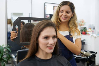 Kuaför, müşterinin fön çektikten sonra kafasının arkasını görebilmesi için küçük bir ayna kullanıyor.