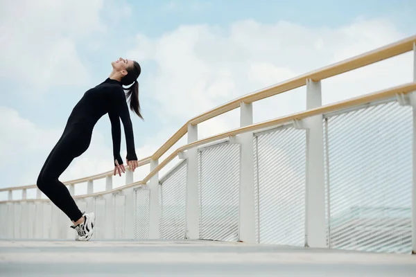 穿着黑色连衣裙的快乐的女舞蹈演员站在桥上 — 图库照片