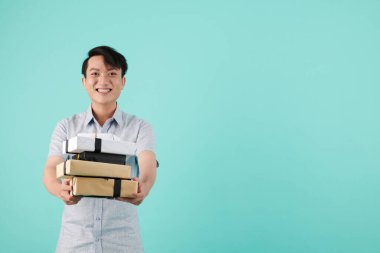 Neşeli heyecanlı genç adam elinde hediyeler, hediyeler ve kameraya gülümsüyor.