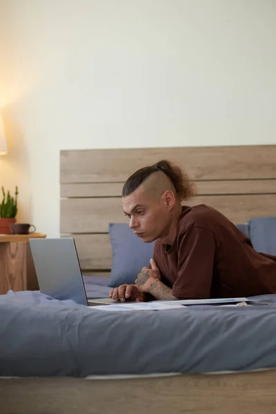 Ciddi Bir Genç Adam Yatakta Uzanıyor Dizüstü Bilgisayardaki Belgeleri Okuyor — Stok fotoğraf