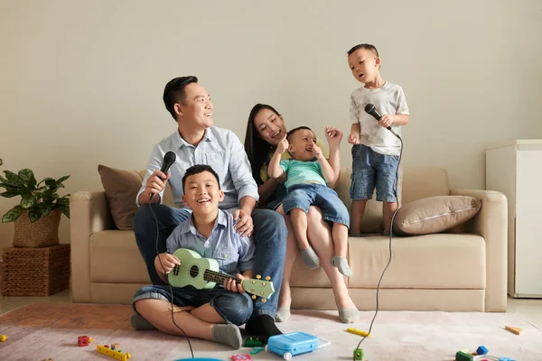 5つの笑いの幸せなアジアの家族は ウクレレを演奏し マイクに歌を歌う — ストック写真