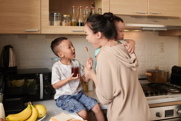 Malý Syn Sedí Kuchyňské Lince Dává Matce Lžičku Marmelády Ochutnat — Stock fotografie