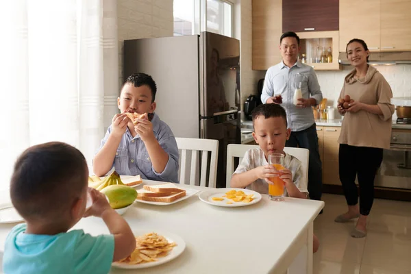 快乐的父母看着他们的三个儿子在厨房餐桌边吃早餐 — 图库照片