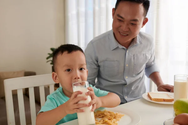 幸せな父見ますザ小さな息子飲むガラスの上の全体のミルクで朝食テーブル — ストック写真