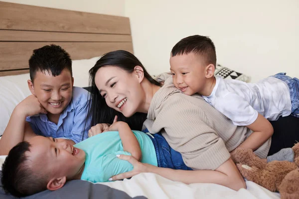 笑着妈妈和她的三个儿子在床上玩耍 互相爱抚 — 图库照片