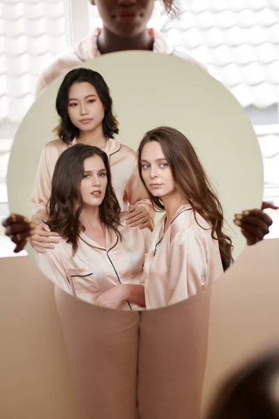 絹のピンクのパジャマで3人の若い女性の反射とラウンドミラーを保持女性 — ストック写真