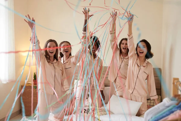 Yatakta Dikilmiş Ipek Pijamalı Plastik Kurdelelerle Kollarını Kaldıran Heyecanlı Kızlar — Stok fotoğraf