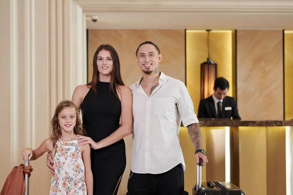 ホテルのホールに立つスーツケース付きの陽気な家族 — ストック写真