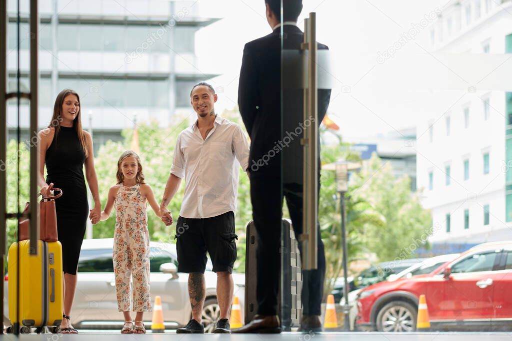 Happy family of three standing at hotel entrance doors
