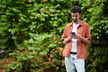Gülümseyen adam dışarıda duruyor ve kız arkadaşından mesaj okuyor.