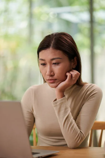 在手提电脑屏幕上阅读电子邮件或文章的年轻而敏感的亚洲女人 — 图库照片