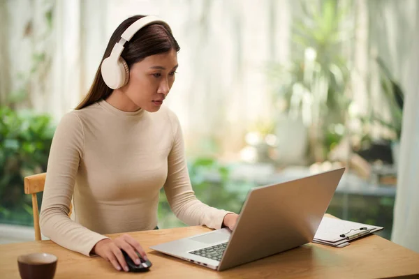 年轻妇女在笔记本电脑上工作时戴着耳机 从同事那里打听电子邮件 — 图库照片