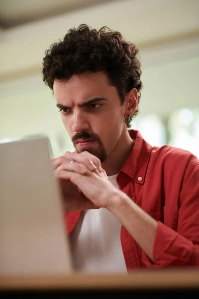 皱眉的男人看着笔记本电脑屏幕上的程序代码 — 图库照片