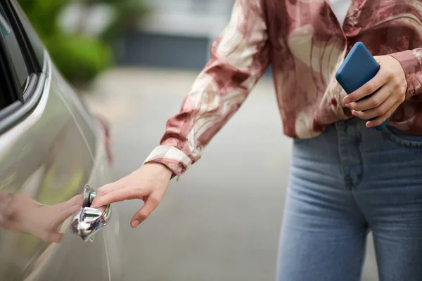 タクシーのドアを開ける手にスマートフォンを持つ女性の作物のイメージ — ストック写真