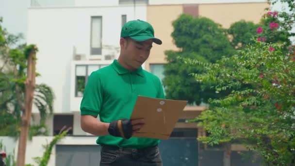 身穿绿色制服 戴着手套的亚洲送货人打电话给客户 约定会面 在街上送包裹 — 图库视频影像