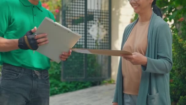 亚洲妇女从身穿绿色制服的送货男子手中接过包裹 并在大门附近屋外签字收件的剪影 — 图库视频影像