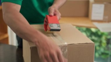 Adamın yapışkan bantla kutu paketleyip posta pulunu dışarı attığı yakın plan.