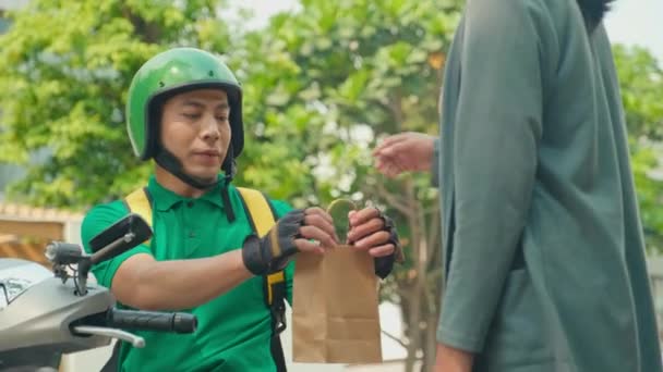 身着绿色制服 头戴摩托车头盔的送货员在屋外给女客户提包的中型照片 — 图库视频影像