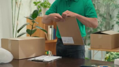 Ofisteki müşteriye göndermeden önce yeşil üniformalı bir postacı zarfta belge paketliyor ve üzerine adres yazıyor.