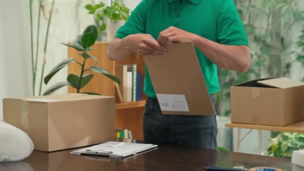 封筒に緑の統一包装文書の郵便労働者とオフィスで顧客に出荷する前にそれに住所を書く — ストック動画