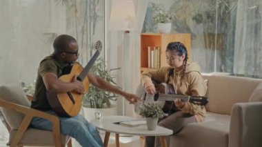 Müzik öğretmeni ve genç öğrencisi oturma odasında yeni gitar çalmayı öğreniyorlar.