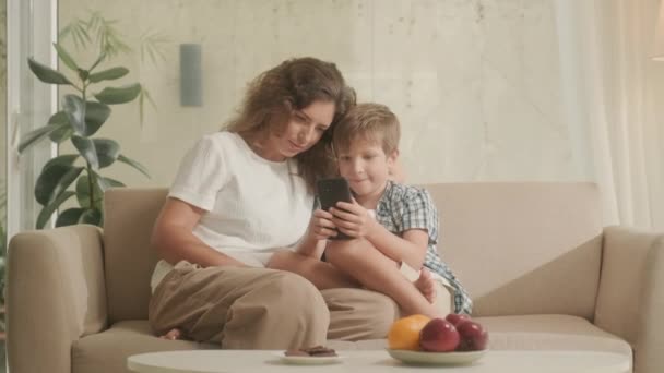 母亲和儿子坐在客厅的沙发上 用智能手机上网 — 图库视频影像