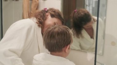 Genç anne küçük oğluna havlu veriyor. Lavaboda yüzünü yıkıyor.