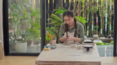 Atölyedeki masada kilden figürler şekillendirirken orta boy kadın resmi.