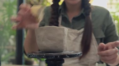 Bir kadının atölyede süngerle kil çömleği ıslatırken görüntüsü.