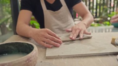 Kadın ve erkek kil figürleri yontuyor ve atölyede masa başı işliyor.