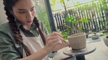 Asya 'lı bir kadının atölyede çömlek çarkında killi çömlek şekillendirirken orta boy bir fotoğrafı.