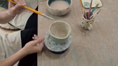 Stüdyoda çömlek çarkının üzerindeki killi kupaları boyayan ellerin açılı görüntüsünü göster